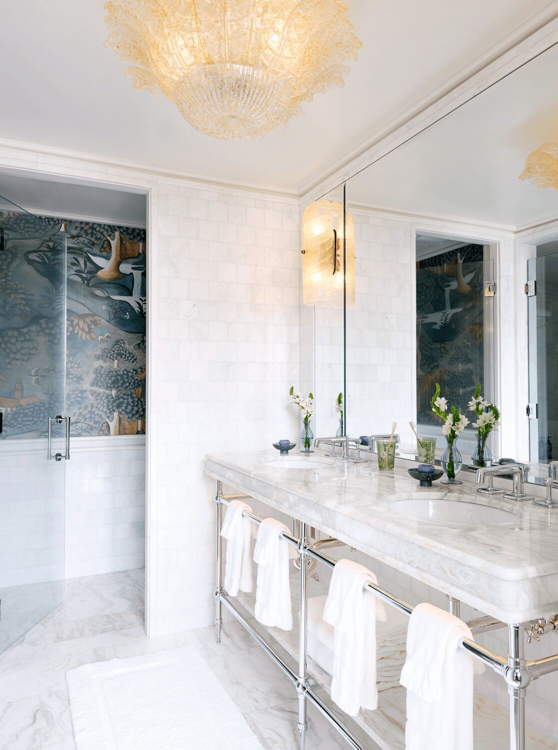 Un baño moderno con tocador de mármol, cabina de ducha de vidrio y una lámpara de techo decorativa.