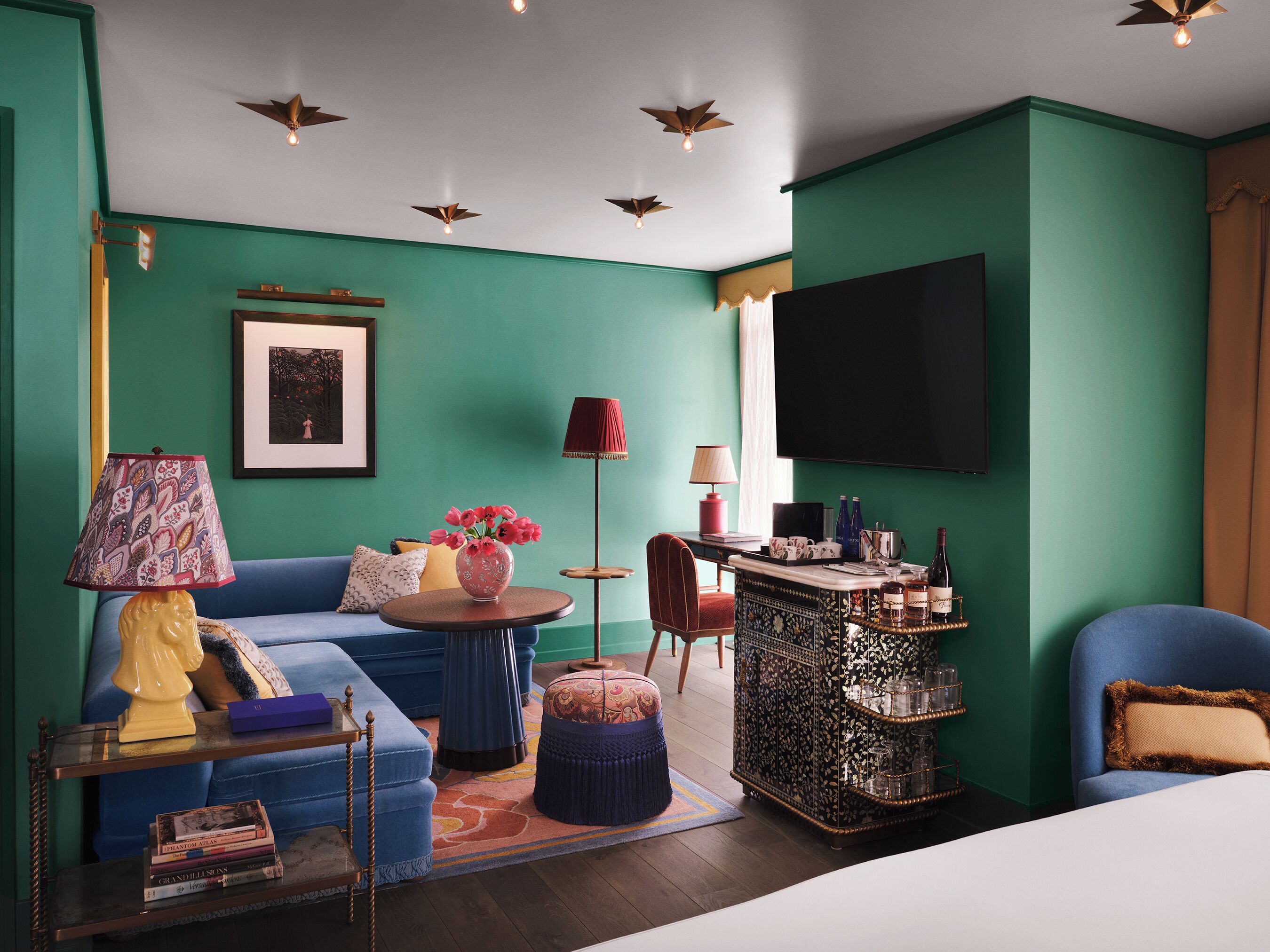Una sala de estar moderna con paredes verde azulado, un sofá azul, una mesa de centro y un televisor montado en la pared.
