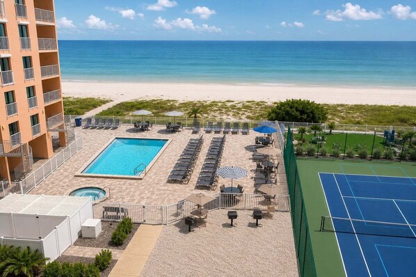 Un complexe hôtelier doté d’une piscine, de chaises longues, d’un court de tennis et offrant une vue sur la plage et l’océan.
