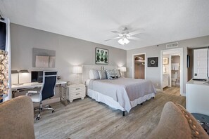 Une chambre à coucher comprenant un lit, un bureau, une chaise, des tables de chevet et un ventilateur de plafond.