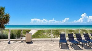 A beach view with a fence, a trash can, and lounge chairs. - 🌊Beachfront Paradise: 3BR Condo with Pool & Balcony in Indian Rocks Beach-RC 309! (Indian Rocks Beach)