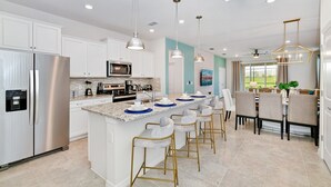 A modern kitchen with stainless steel appliances, a central island with bar stools, pendant lighting, and a view to the outdoors.