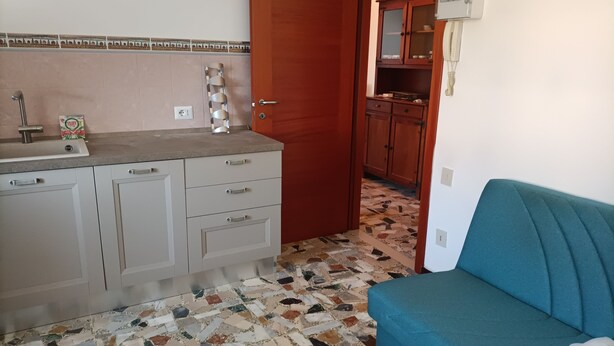 A kitchen with a tiled floor, a sink, and cabinets. There is a wooden door leading to another room. - Renovated apartment in central area (Oristano)