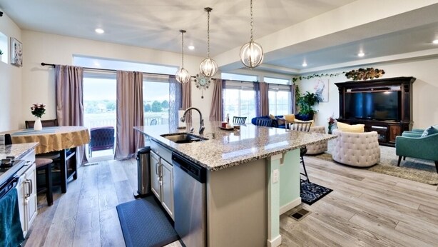 Una cocina moderna con una isla central, un comedor con mesa y sillas, una sala de estar con sofá y televisor, y un amplio ventanal con cortinas.
