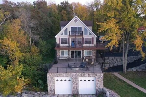 A two-story house with a stone foundation, a balcony on the upper floor, and a garage with two doors. - Tripoli Shores Riverfront Retreat (Cape Vincent)