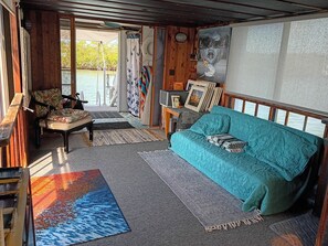 A cozy room with a teal sofa, a wooden chair, and a small table. There is a view of a body of water through the open door. - Island Sanctuary Islamorada (Tavernier)