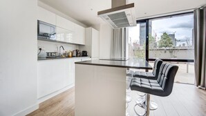 Eine moderne Küche mit einer zentralen Kochinsel, Barhocker und einem großen Fenster mit Blick auf die Stadt.
