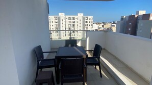 A balcony with a table and chairs, a clear view of buildings in the background, and a tiled floor. - Appartement S1 Avec Grande Terrasse à 10 min de la Plage (Mrezga)