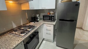 A compact kitchen with a gas stove, oven, microwave, and refrigerator. - Appartement S1 Avec Grande Terrasse à 10 min de la Plage (Mrezga)