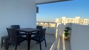 A balcony with a table and chairs, a potted plant, and a view of buildings in the distance. - Appartement S1 Avec Grande Terrasse à 10 min de la Plage (Mrezga)