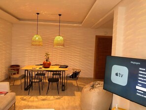Ett modernt vardagsrum med en matplats, där en stor platt-TV visar Apple TV-gränssnittet.