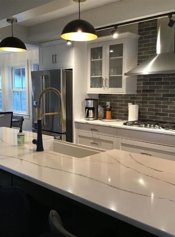 A modern kitchen with white cabinets, a stainless steel refrigerator, a gas stove, and pendant lighting.