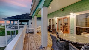 A covered outdoor deck with a dining table and chairs, a covered seating area, and a view of the ocean.