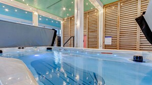 A hot tub with a wooden wall backdrop, a ceiling with string lights, and a visible safety sign.