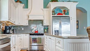 A spacious kitchen with white cabinetry, a stainless steel refrigerator, a stove, and a chandelier.