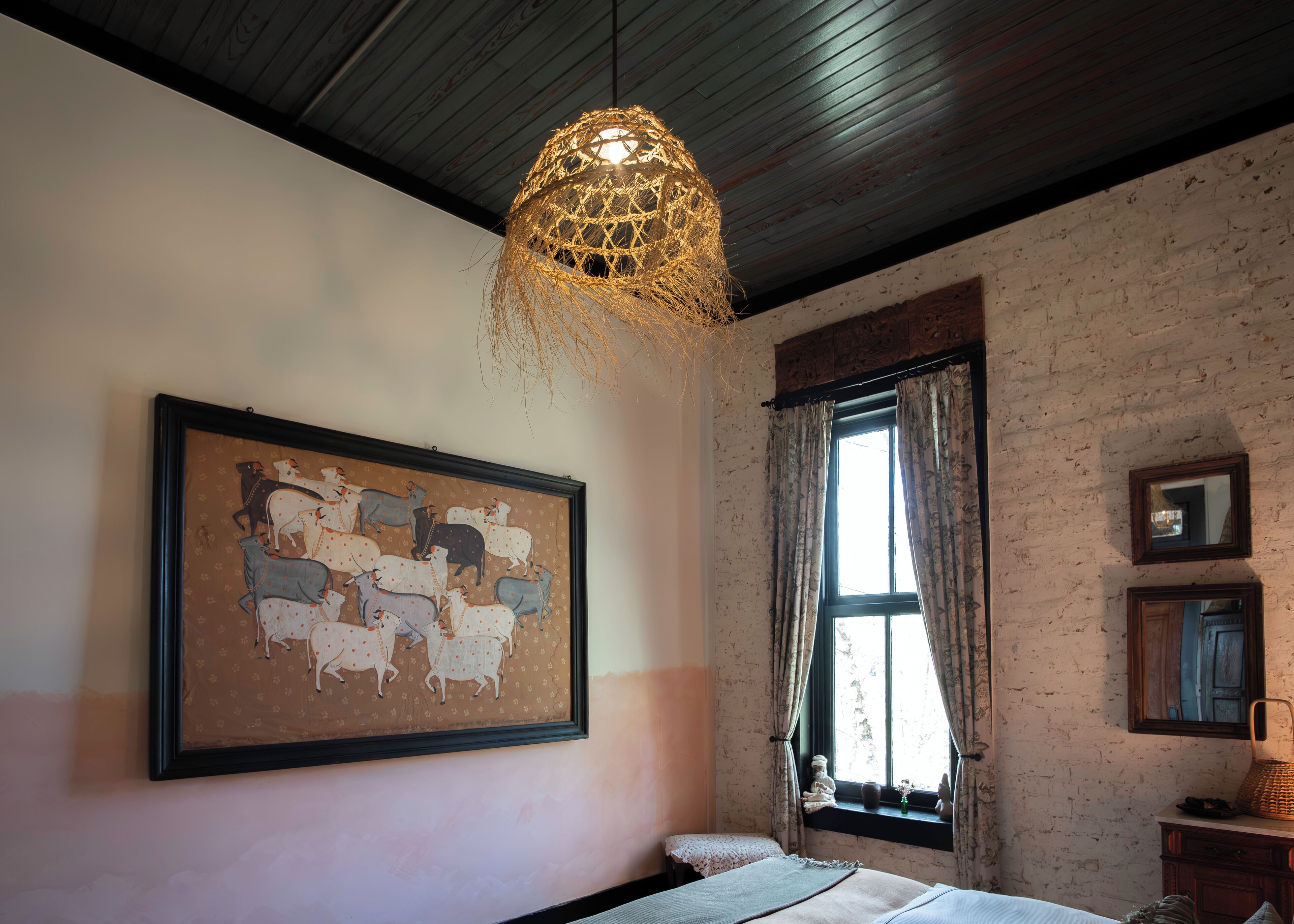 A bedroom with a bed, a framed animal painting, a window with curtains, and a hanging light fixture.
