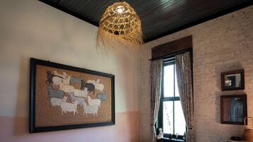 A bedroom with a bed, a framed animal painting, a window with curtains, and a hanging light fixture.