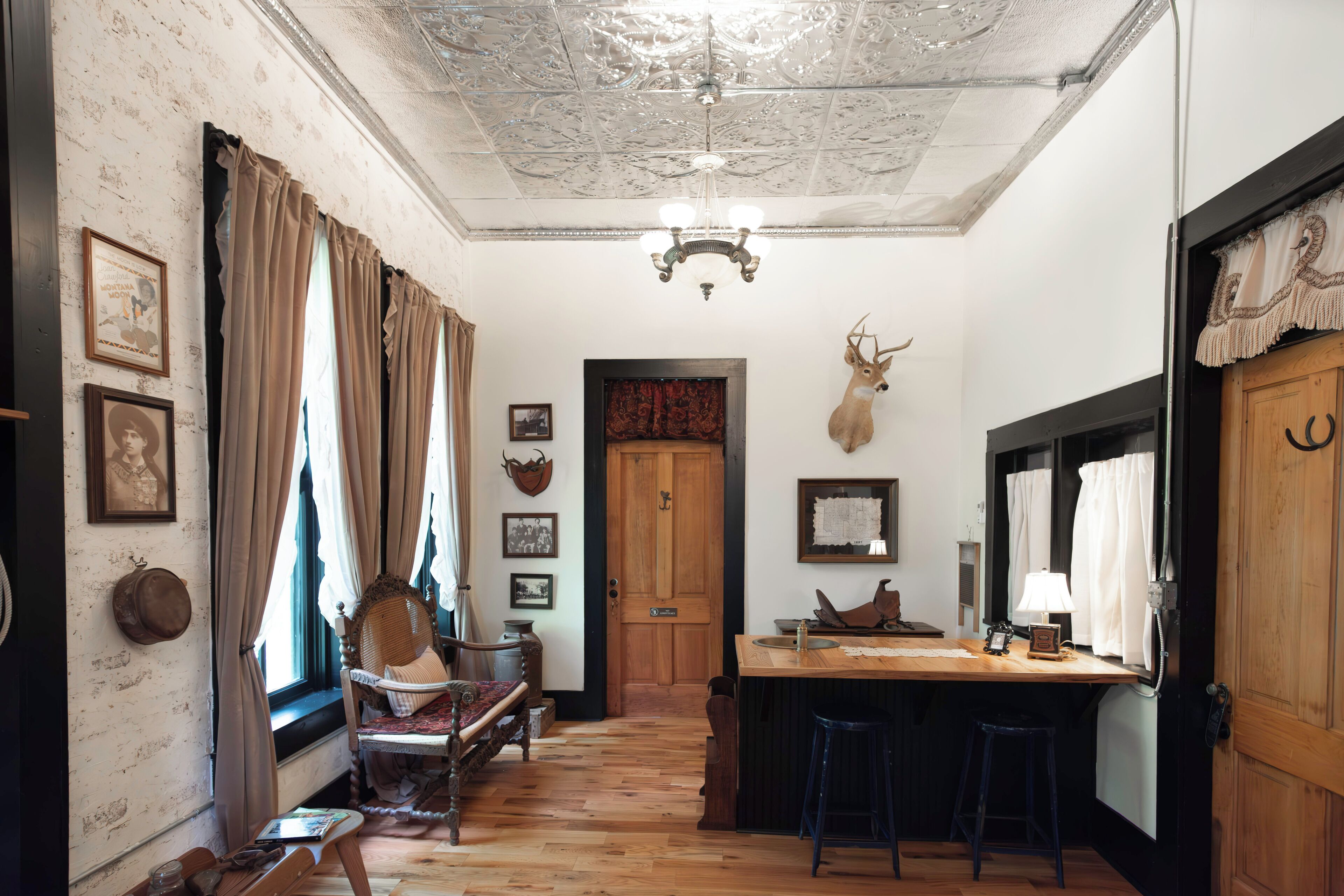 A rustic interior with a wooden ceiling, a chandelier, a deer head mounted on the wall, and a wooden door.