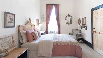 A bedroom with a bed, a nightstand, a dresser, a mirror, and a window with curtains.