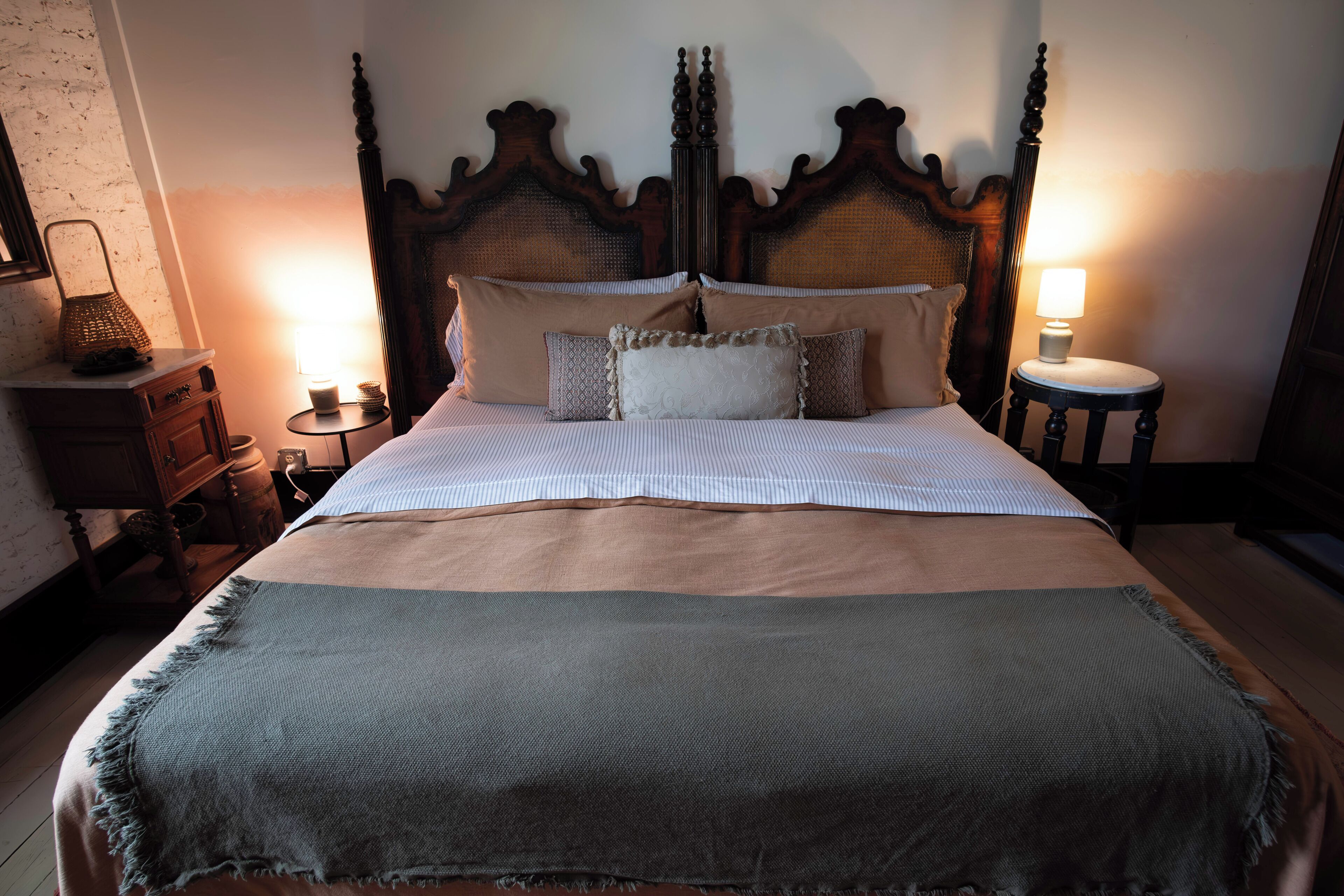 A neatly made bed with a wooden headboard, two bedside tables with lamps, and a small wooden nightstand with a lamp.