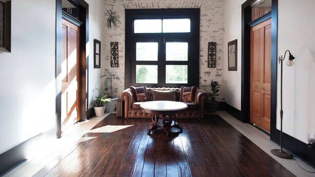 A room with a wooden floor, a round table, a brown sofa, and two doors. - Beard and Lady Inn (Chester)