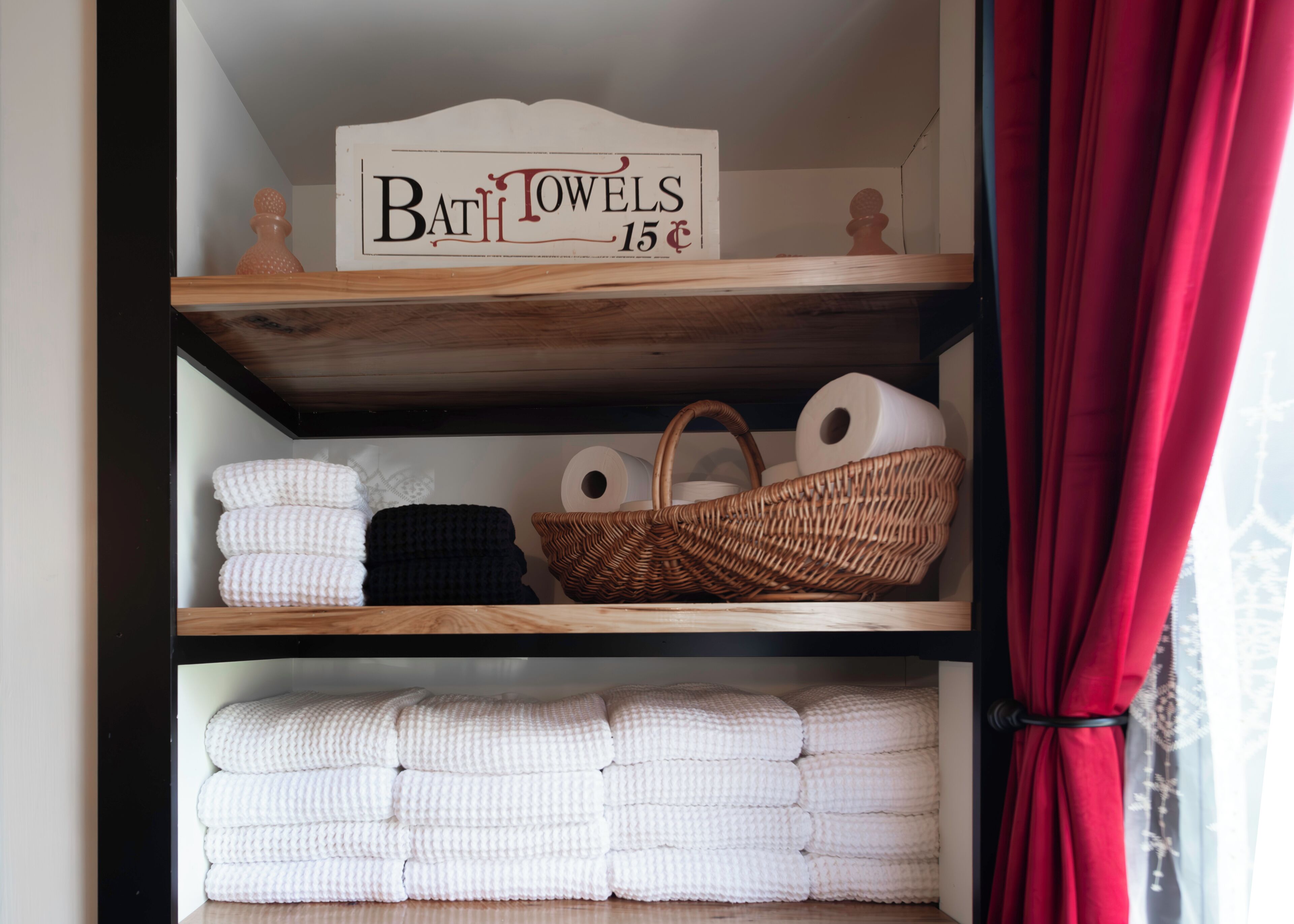 Une étagère avec des serviettes de bain, un panneau indiquant « Serviettes de bain 15 € » et un panier.