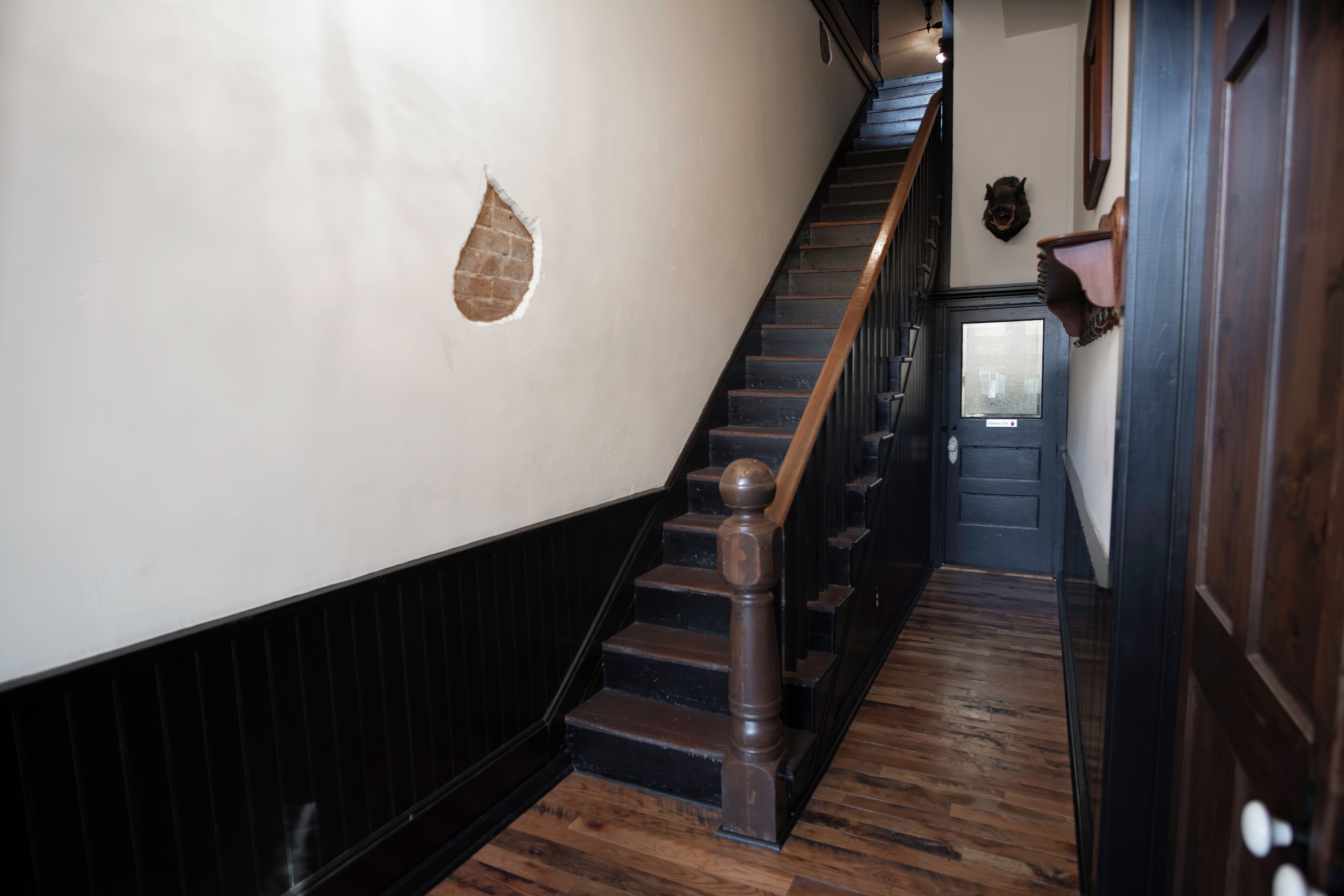 A wooden staircase with a handrail, a dark wooden floor, and a white wall with a small hole.