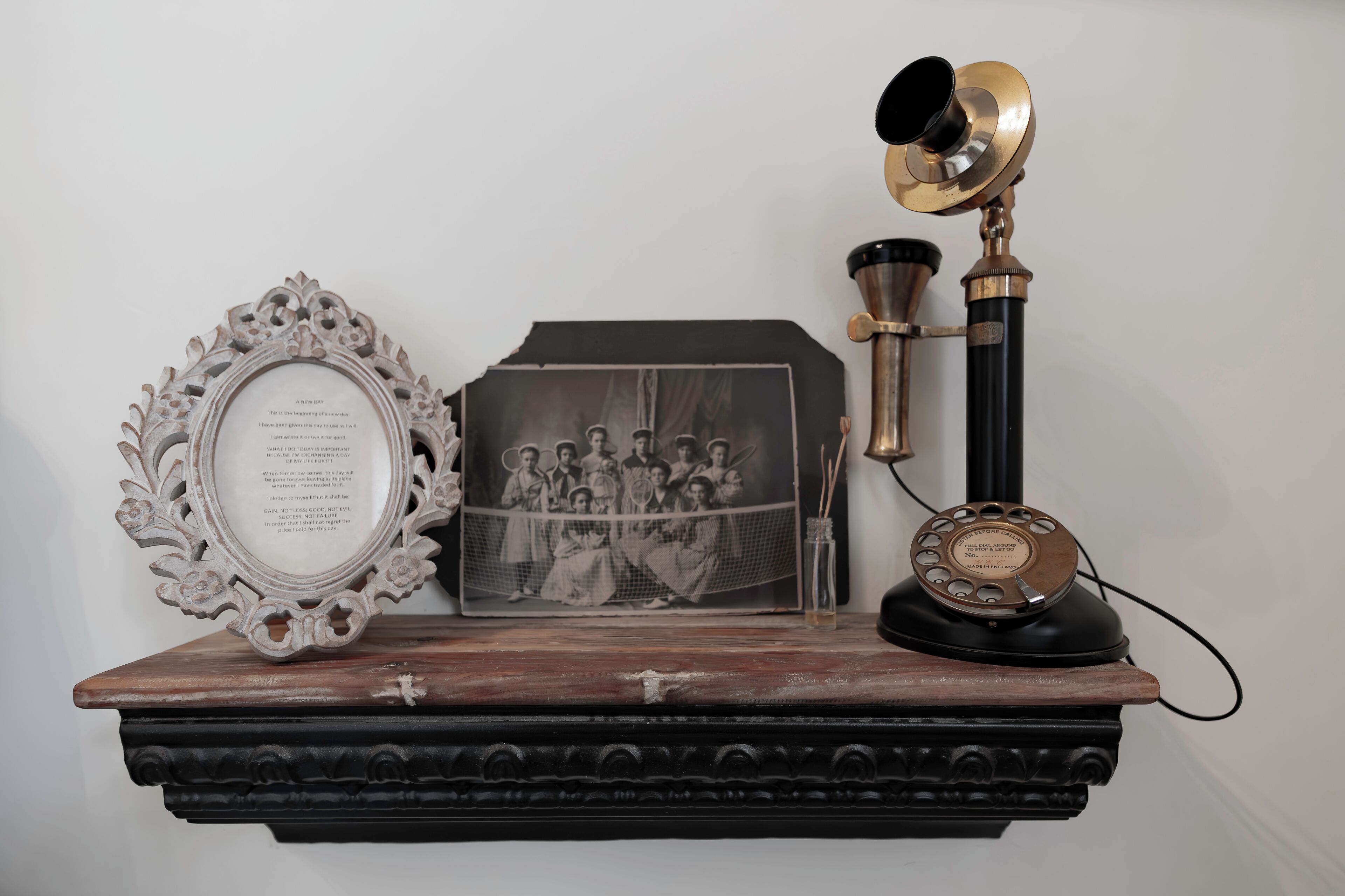A wooden shelf with a framed photograph, a decorative mirror, and a vintage telephone.