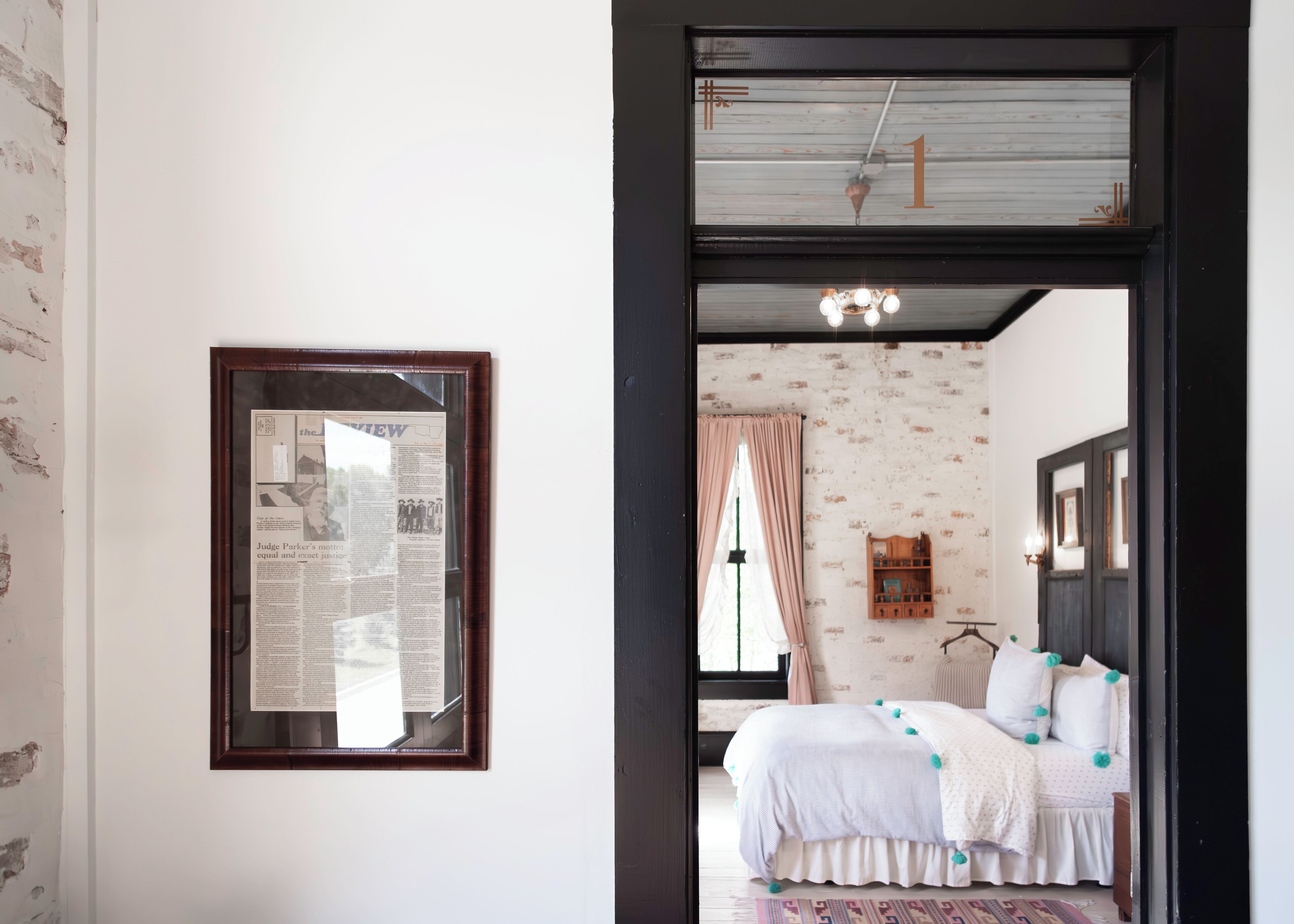A bedroom with a bed, a wooden headboard, a window with curtains, and a framed newspaper on the wall.