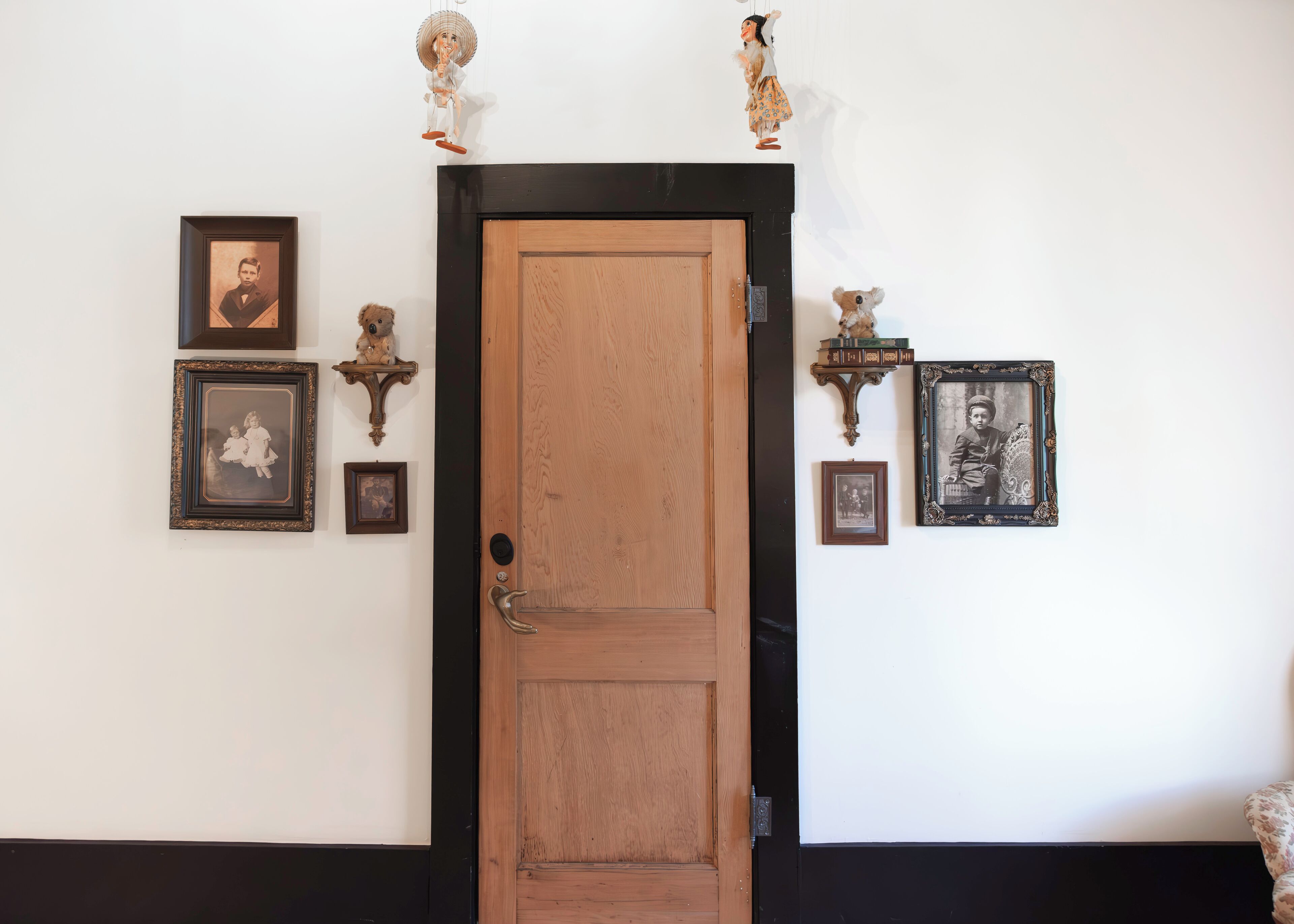 Una puerta de madera con marco negro, flanqueada por dos estantes empotrados con fotografías enmarcadas y pequeños adornos.
