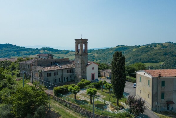 A historic building with a bell tower, surrounded by lush greenery and a hilly landscape.