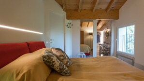 A bedroom with a bed, a red headboard, a wooden ceiling, a window, and a bathroom visible through an open door. - GuestHost - Cozy apartment that hosts up to 4 people, located in a shared villa in the hilly Umbrian countryside. We are in the Ponte Rio hamlet, an extremely quiet and relaxing area in which to stay in close contact with nature but at the same time not  (Perugia)
