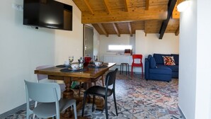A dining area with a wooden ceiling, a TV mounted on the wall, a dining table with chairs, and a patterned floor. - GuestHost - Cozy apartment that hosts up to 4 people, located in a shared villa in the hilly Umbrian countryside. We are in the Ponte Rio hamlet, an extremely quiet and relaxing area in which to stay in close contact with nature but at the same time not  (Perugia)