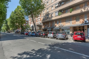 A street with parked cars, a building with a sign for 'SANTARI ELETROMEDICO,' and trees lining the road.