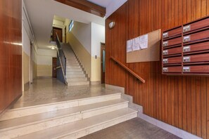 A staircase leading to an upper floor, wooden panel walls, a bulletin board, and a row of mailboxes.
