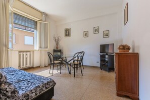 A bedroom with a bed, a window with blinds, a table with chairs, a TV, and a cabinet.