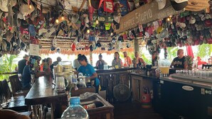Una zona de bar con mostrador de madera, varias botellas y un ventilador.
