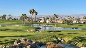 A golf course with a pond, palm trees, and mountains in the background. - Newly upgraded throughout and GORGEOUS sunset and mountain views! (Palm Desert)