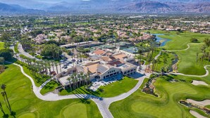 An aerial view of a golf course with a clubhouse, surrounded by residential areas and mountains in the background. - Newly upgraded throughout and GORGEOUS sunset and mountain views! (Palm Desert)
