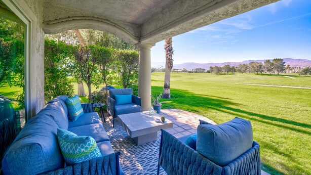 A covered patio with a sofa set, a coffee table, and a view of a well-manicured lawn and distant mountains. - Newly upgraded throughout and GORGEOUS sunset and mountain views! (Palm Desert)