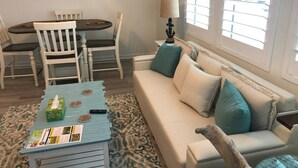 Una sala de estar con un sofá, una mesa de centro, una mesa de comedor con sillas, una lámpara y una ventana con persianas.