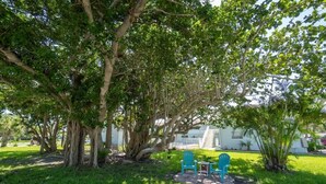 A lush garden with large trees and a seating area with two chairs and a table. - Cape Canaveral Condo w/Pool, Steps to Beach Access (Cape Canaveral)