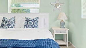 A bedroom with a bed, two patterned pillows, a blue blanket, a nightstand with a lamp, and a wall decoration. - Cape Canaveral Condo w/Pool, Steps to Beach Access (Cape Canaveral)