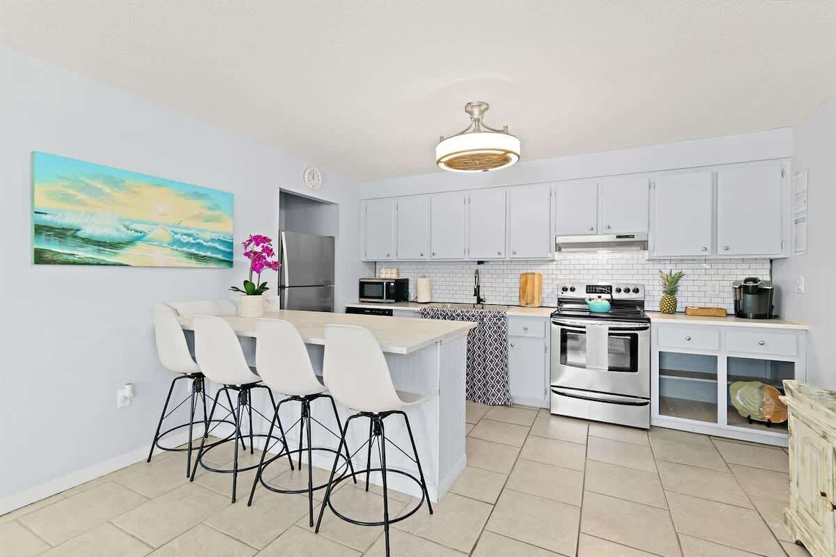 A modern kitchen with white cabinets, a central island with bar stools, stainless steel appliances, and a ceiling light fixture.