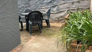 A small outdoor seating area with a table and chairs, a potted plant, and a stone wall. - Piano Coliving POA (Porto Alegre)