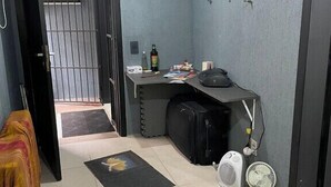 A room with a desk, a chair, a suitcase, a fan, and a door leading to a hallway. - Piano Coliving POA (Porto Alegre)