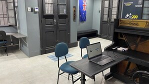 A modern office space with a laptop on a desk, two blue chairs, a flag, and a plaque on the wall. - Piano Coliving POA (Porto Alegre)