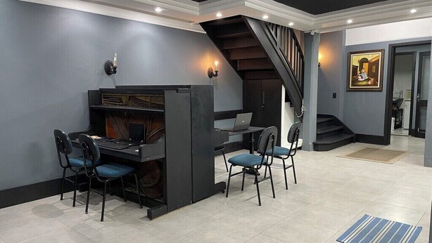 A modern interior with a piano, a laptop on a desk, and a staircase. - Piano Coliving POA (Porto Alegre)