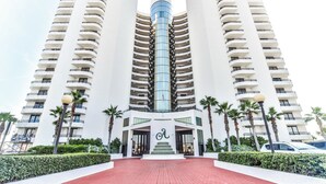 Un hotel moderno con una torre central de vidrio, varios balcones y una entrada de ladrillo rojo.