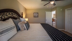 Une chambre à coucher comprenant un lit, un ventilateur de plafond, une lampe, une porte et un couloir menant à une autre pièce.